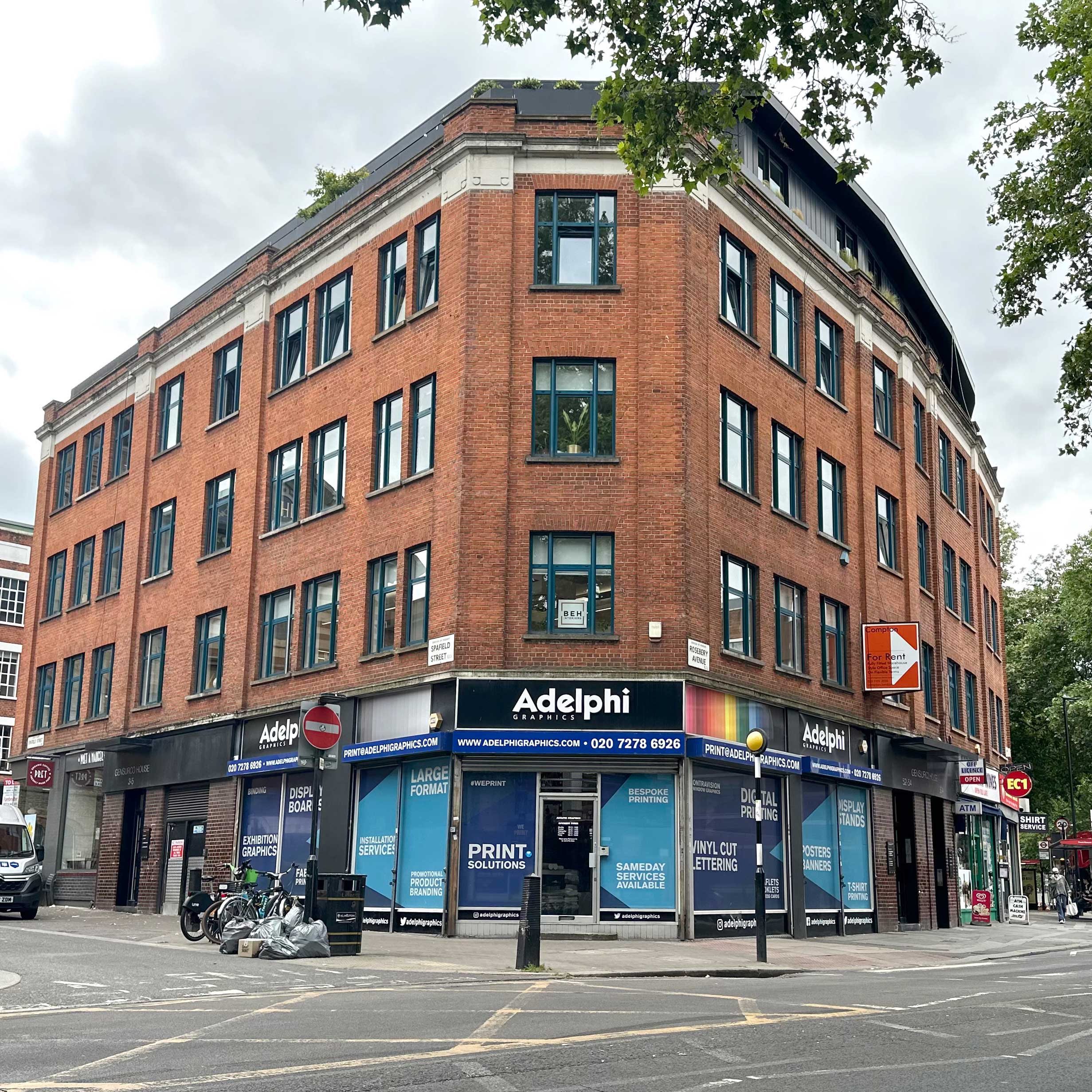 Corner view of a red-brick commercial building in London housing Adelphi Graphics, located at 9-10 Charterhouse Buildings, with large windows and ground-floor signage.